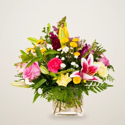Flower arrangement in vase with lilies, roses and carnations in a glass cube